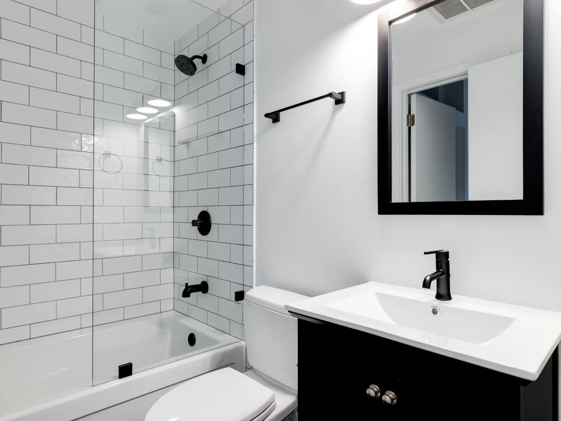 Freshly cleaned bathroom with a glass shower screen, white tile and black fixtures